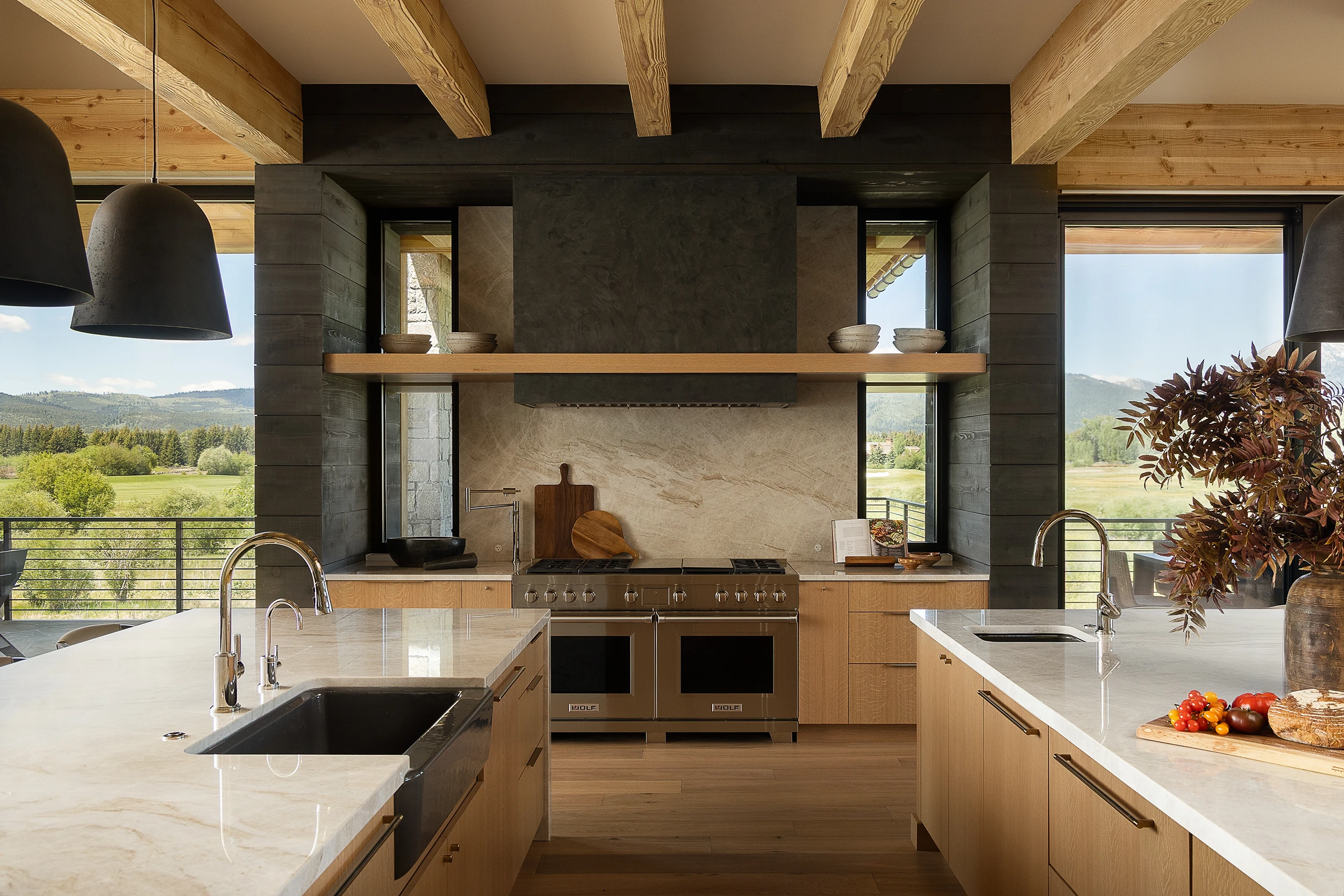Custom white oak kitchen cabinetry with dual stone-topped islands, professional range, exposed wood beams, and mountain views.