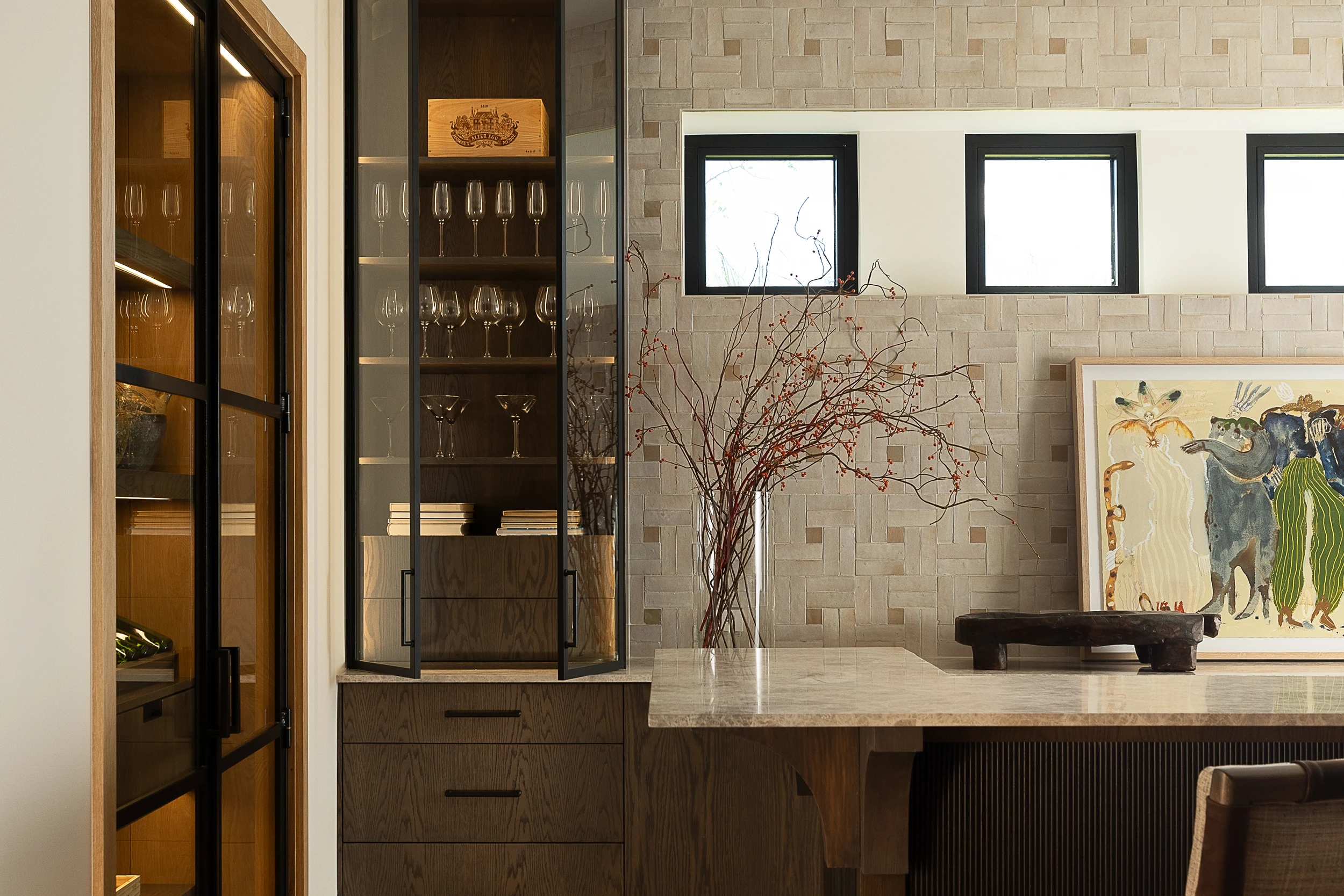 A bold and stylish bathroom featuring vibrant orange and white patterned wallpaper. The dark green vanity with a warm wooden countertop contrasts beautifully with the bright backdrop. A sculptural white vessel sink sits beneath a gold faucet, adding a touch of elegance. The brass hardware and wall-mounted light fixture enhance the vintage-inspired aesthetic.