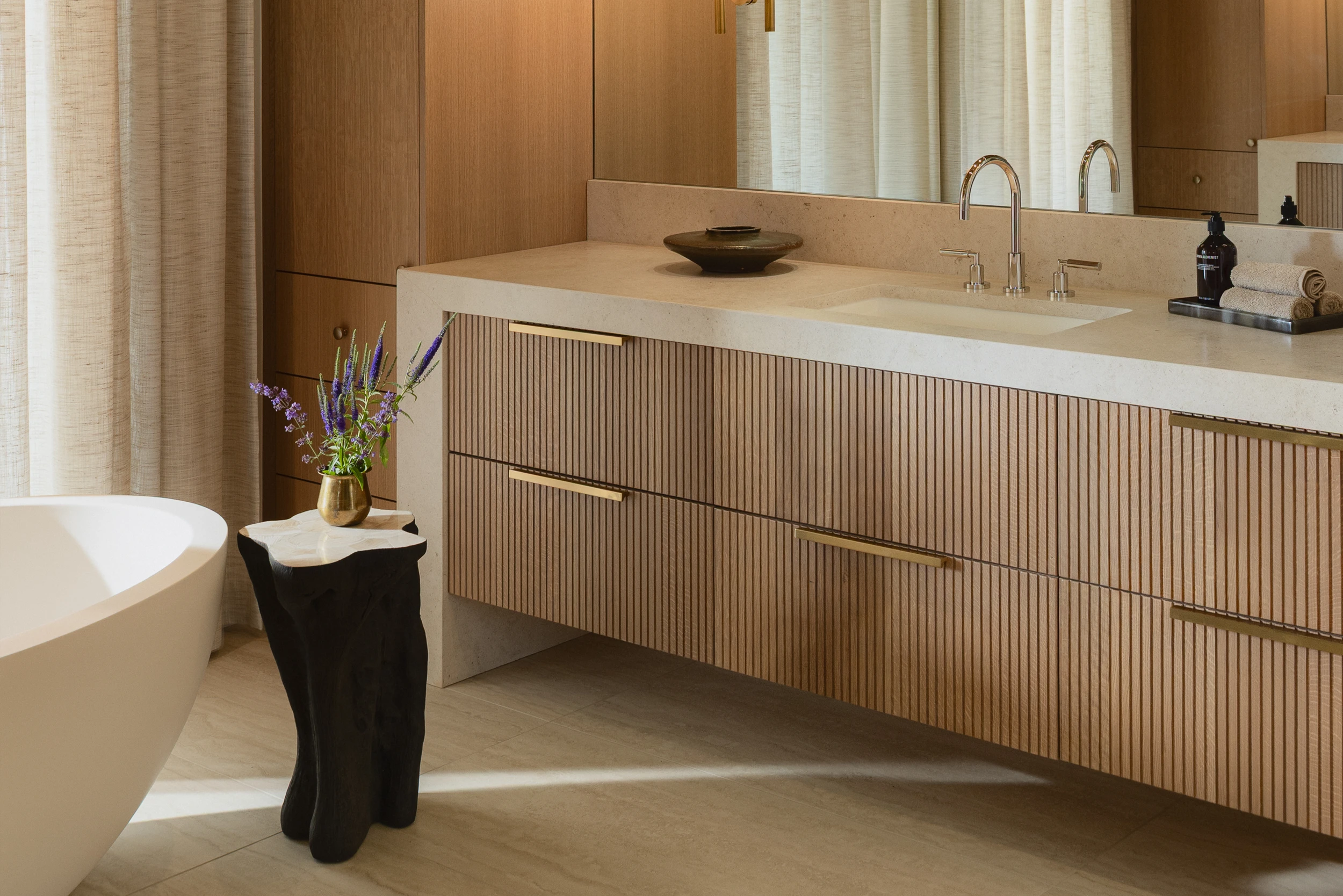 A bold and stylish bathroom featuring vibrant orange and white patterned wallpaper. The dark green vanity with a warm wooden countertop contrasts beautifully with the bright backdrop. A sculptural white vessel sink sits beneath a gold faucet, adding a touch of elegance. The brass hardware and wall-mounted light fixture enhance the vintage-inspired aesthetic.